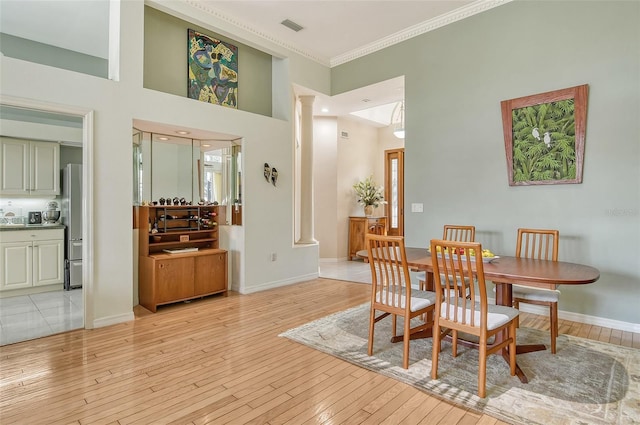 dining room with crown molding, a towering ceiling, decorative columns, and light hardwood / wood-style flooring