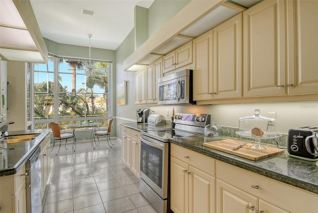 kitchen with sink, hanging light fixtures, light tile patterned floors, dark stone counters, and stainless steel appliances