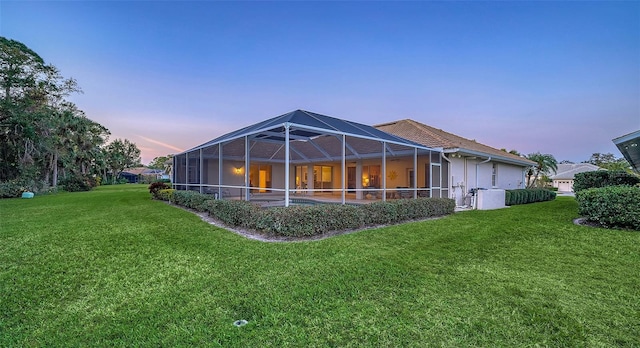 back house at dusk featuring a yard and glass enclosure