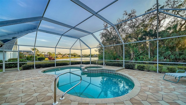 pool at dusk with a patio, an in ground hot tub, and glass enclosure