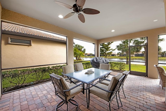 sunroom featuring ceiling fan and a water view