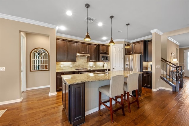 kitchen featuring sink, decorative light fixtures, a center island with sink, appliances with stainless steel finishes, and a kitchen breakfast bar