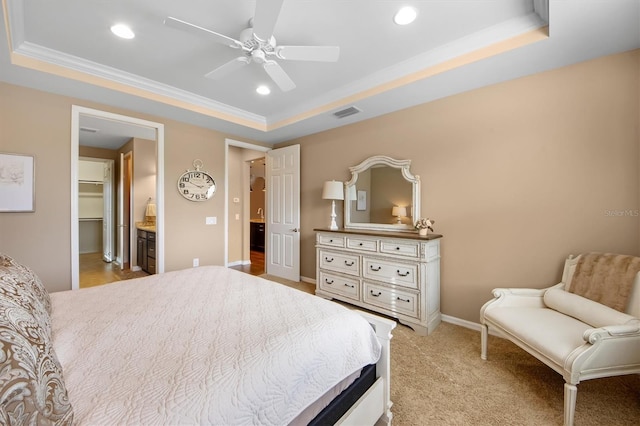 carpeted bedroom with ensuite bathroom, a walk in closet, ornamental molding, a raised ceiling, and ceiling fan