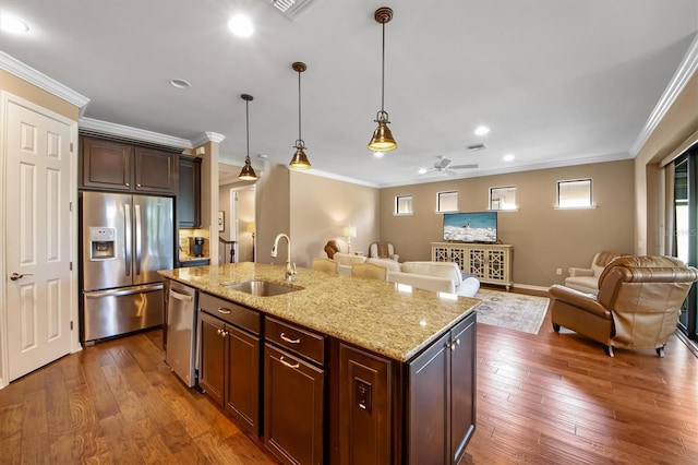 kitchen with sink, appliances with stainless steel finishes, a kitchen island with sink, hanging light fixtures, and light stone countertops