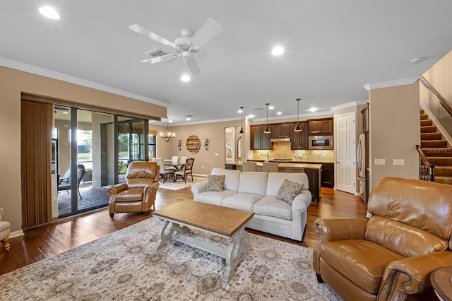 living room with crown molding, dark wood-type flooring, and ceiling fan with notable chandelier