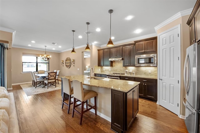 kitchen with appliances with stainless steel finishes, pendant lighting, an island with sink, dark wood-type flooring, and dark brown cabinets