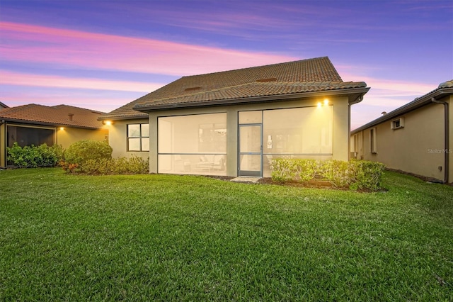 back house at dusk with a sunroom and a yard