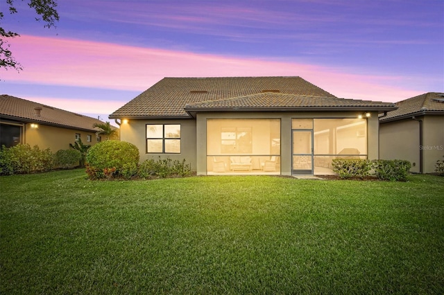 back house at dusk featuring a yard and a sunroom