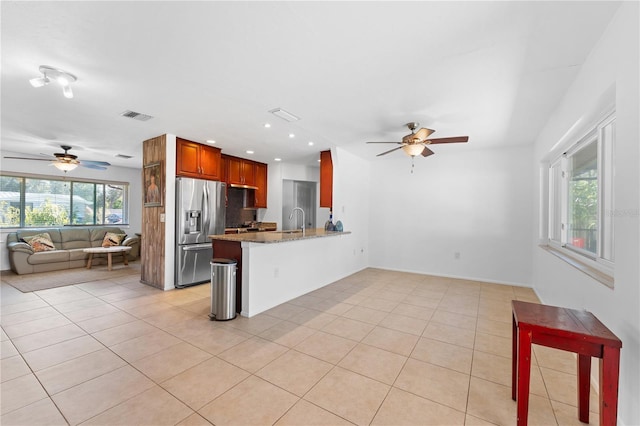 kitchen featuring plenty of natural light, stainless steel fridge, kitchen peninsula, and light stone countertops