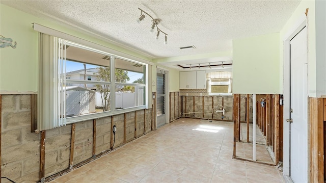 interior space featuring light tile patterned flooring, plenty of natural light, rail lighting, and a textured ceiling