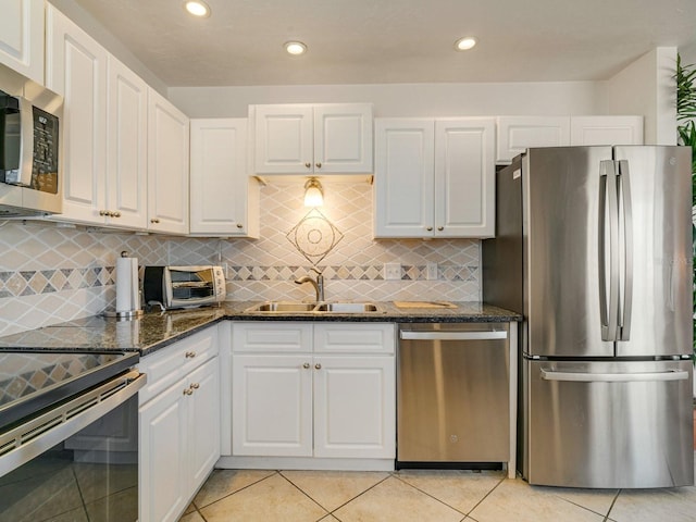 kitchen with light tile patterned flooring, sink, white cabinetry, appliances with stainless steel finishes, and dark stone counters