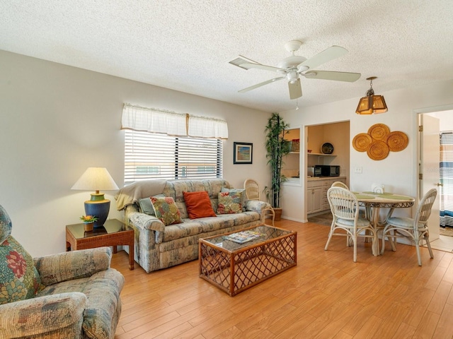 living room featuring ceiling fan, light hardwood / wood-style flooring, and a textured ceiling