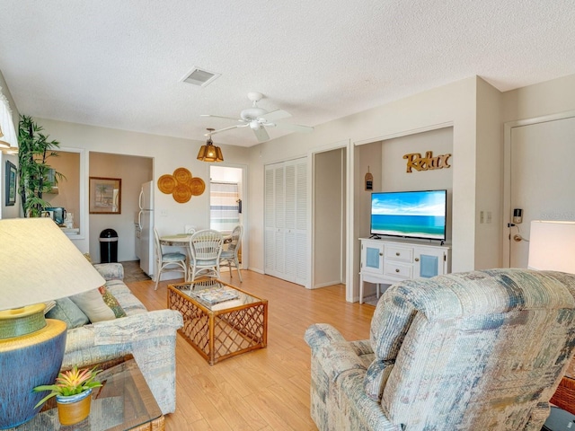 living room featuring ceiling fan, a textured ceiling, and light wood-type flooring