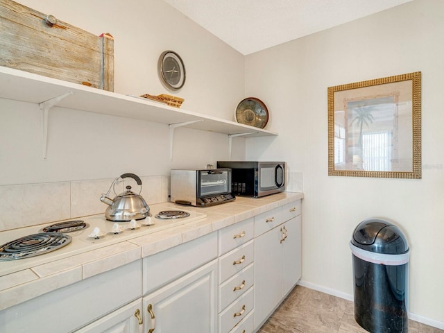 kitchen with white stovetop, tile counters, and white cabinets