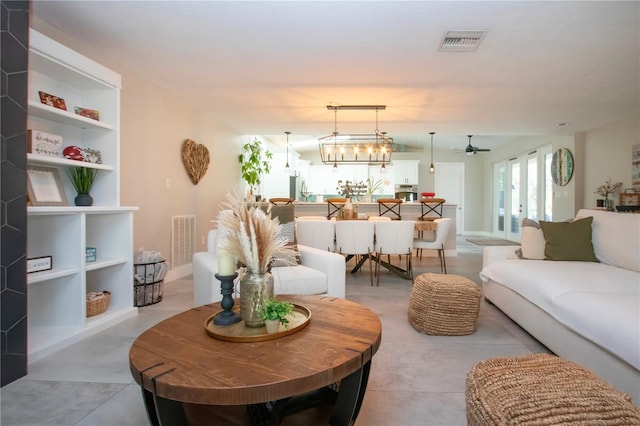 living room with built in shelves, ceiling fan with notable chandelier, and french doors