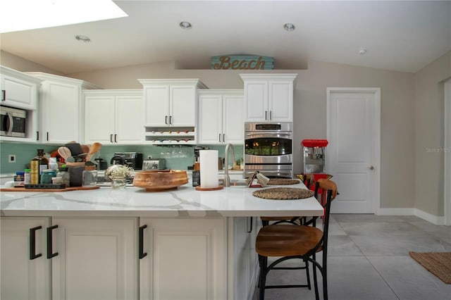 kitchen featuring light stone counters, stainless steel appliances, vaulted ceiling with skylight, and white cabinets