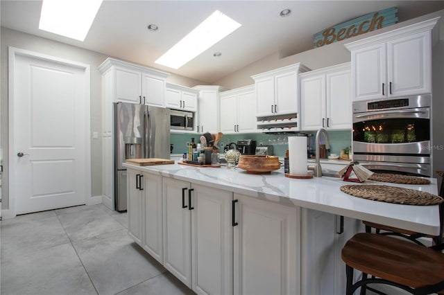 kitchen with white cabinetry, appliances with stainless steel finishes, lofted ceiling with skylight, and light stone counters