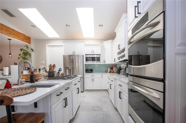 kitchen with sink, appliances with stainless steel finishes, white cabinetry, backsplash, and a skylight