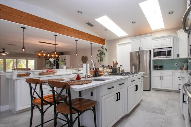 kitchen featuring a breakfast bar, vaulted ceiling with skylight, tasteful backsplash, a kitchen island with sink, and stainless steel appliances