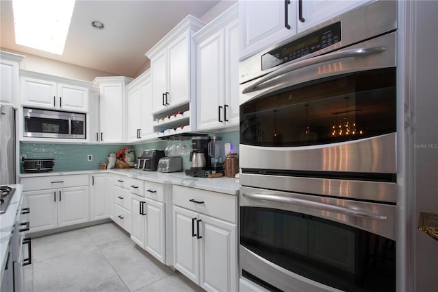 kitchen featuring appliances with stainless steel finishes, light tile patterned floors, white cabinets, and backsplash