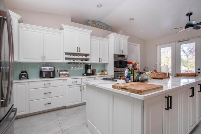 kitchen featuring lofted ceiling, white cabinetry, stainless steel appliances, tasteful backsplash, and a kitchen island