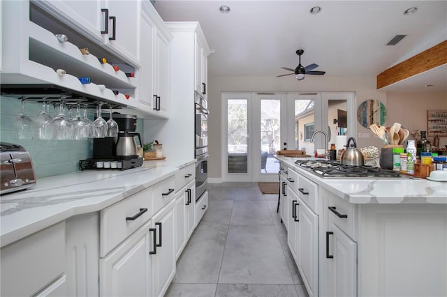 kitchen with ceiling fan, white cabinetry, backsplash, stainless steel appliances, and light stone countertops