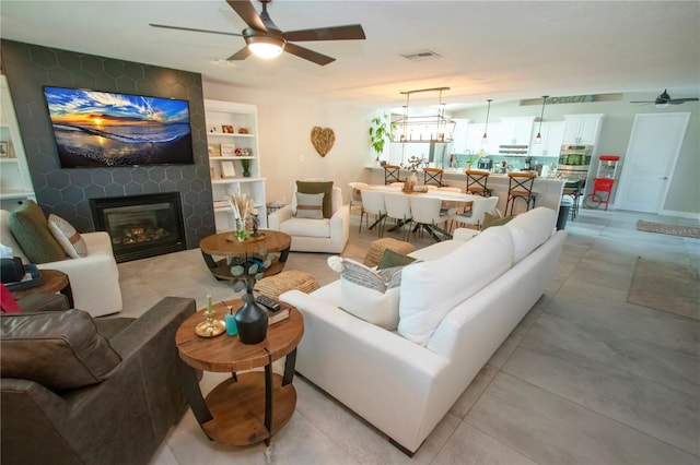 living room featuring a large fireplace and ceiling fan with notable chandelier