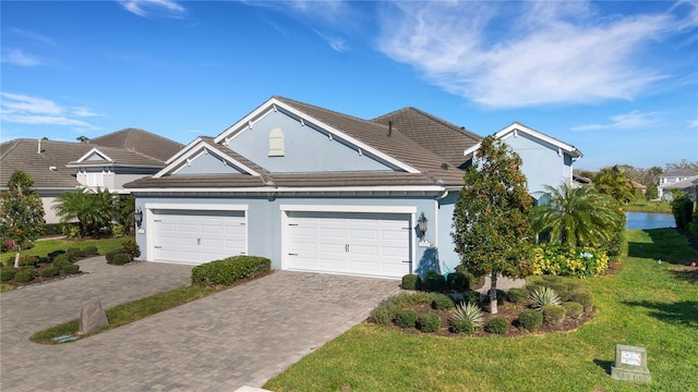 view of front facade featuring stucco siding, a tile roof, decorative driveway, an attached garage, and a front yard