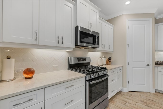 kitchen featuring light stone counters, white cabinets, ornamental molding, appliances with stainless steel finishes, and light wood-type flooring