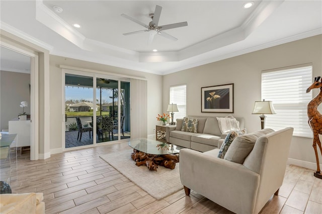 living area with a wealth of natural light, a tray ceiling, wood finish floors, and a ceiling fan