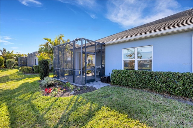 back of property featuring glass enclosure, a lawn, a tiled roof, and stucco siding