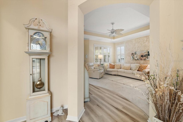 living room featuring crown molding, ceiling fan, a tray ceiling, and light hardwood / wood-style flooring