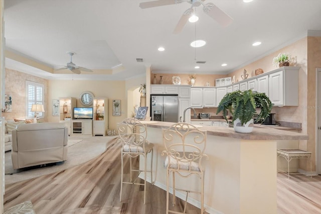 kitchen featuring stainless steel fridge with ice dispenser, white cabinetry, a kitchen bar, ornamental molding, and kitchen peninsula