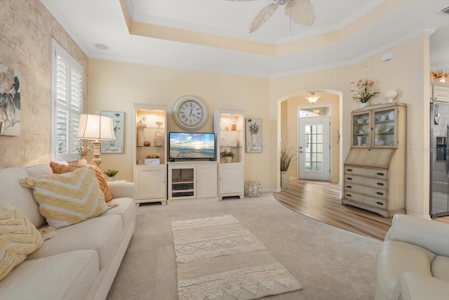 carpeted living room with crown molding, ceiling fan, and a tray ceiling