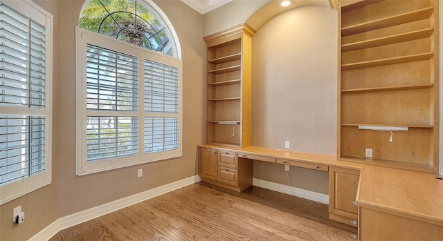 unfurnished office featuring light hardwood / wood-style flooring, built in desk, and a healthy amount of sunlight