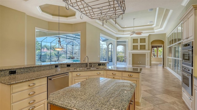 kitchen with sink, a tray ceiling, light stone countertops, and a kitchen island