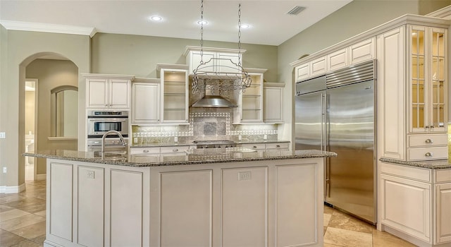 kitchen featuring sink, tasteful backsplash, dark stone countertops, appliances with stainless steel finishes, and an island with sink