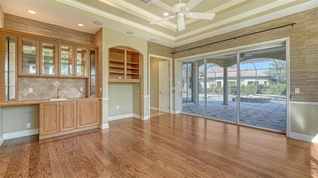 doorway with ceiling fan, ornamental molding, a tray ceiling, and light hardwood / wood-style floors