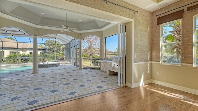 unfurnished sunroom featuring a raised ceiling, plenty of natural light, and ceiling fan