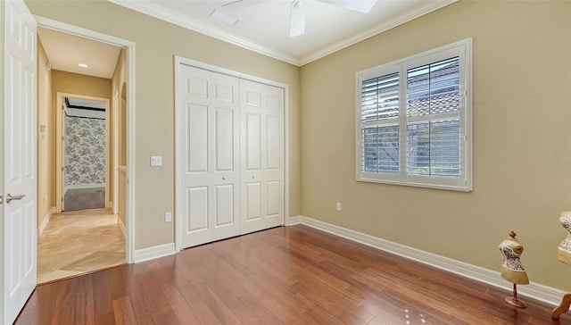 unfurnished bedroom with crown molding, ceiling fan, wood-type flooring, and a closet