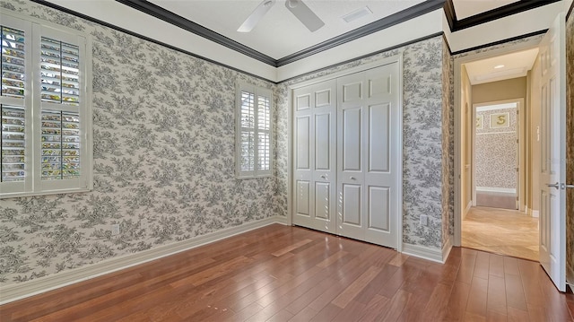 unfurnished bedroom featuring crown molding, wood-type flooring, ceiling fan, and a closet