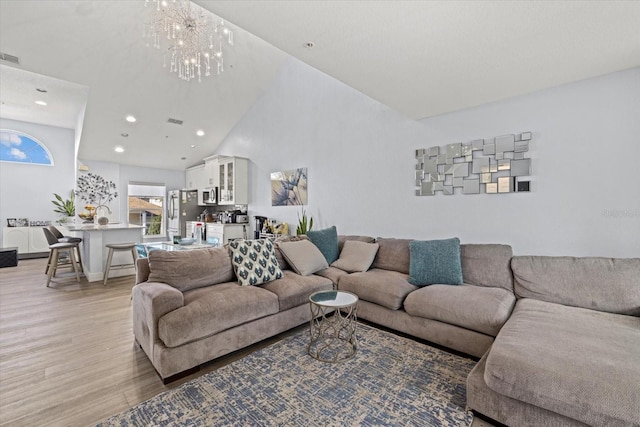 living room with a notable chandelier, high vaulted ceiling, and light hardwood / wood-style flooring