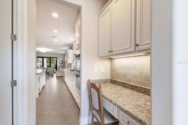 kitchen with white cabinetry, sink, light stone counters, and tasteful backsplash