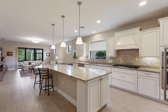 kitchen featuring premium range hood, sink, gas stovetop, light stone counters, and a kitchen island