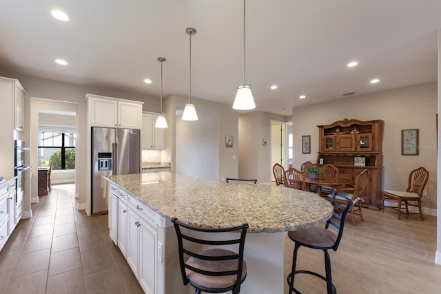 kitchen with high end fridge, white cabinetry, light stone counters, a center island with sink, and decorative light fixtures