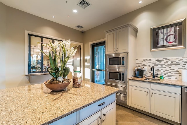 kitchen featuring stainless steel appliances, light stone countertops, sink, and decorative backsplash