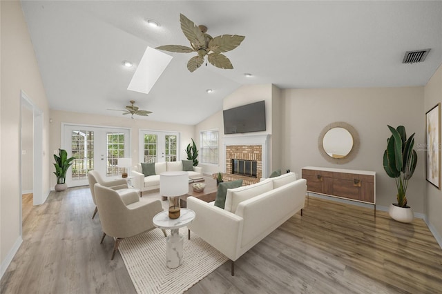 living room featuring french doors, lofted ceiling with skylight, ceiling fan, a fireplace, and light hardwood / wood-style floors