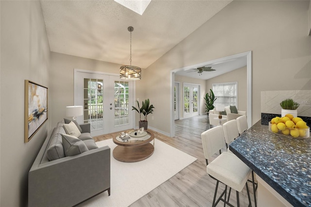 living room featuring light wood finished floors, vaulted ceiling with skylight, french doors, and a healthy amount of sunlight