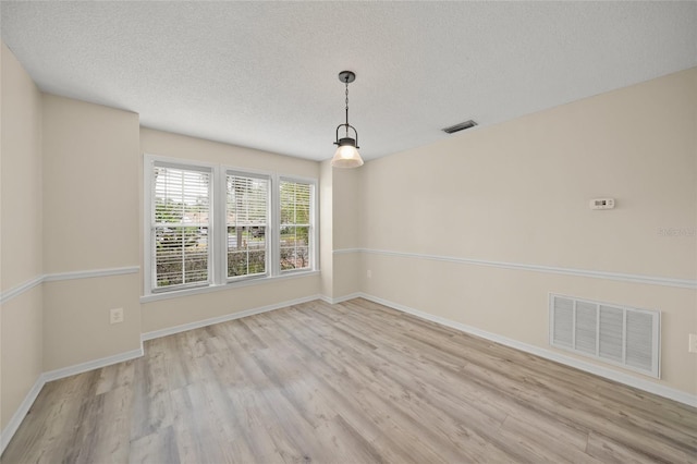 spare room with light wood-type flooring, visible vents, a textured ceiling, and baseboards