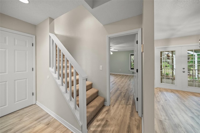 staircase with a textured ceiling, baseboards, wood finished floors, and french doors